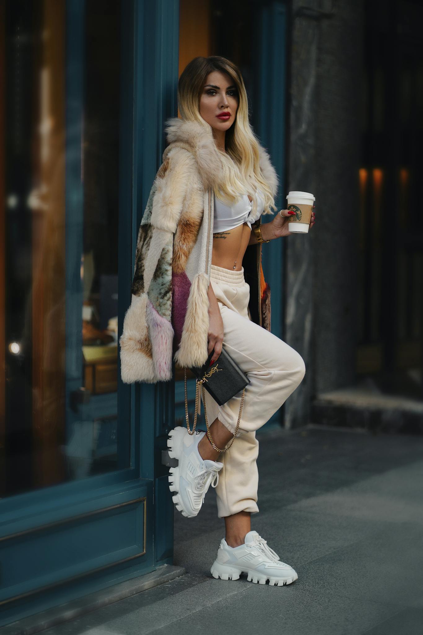 Fashionable woman in urban setting with coffee cup in chic outfit.