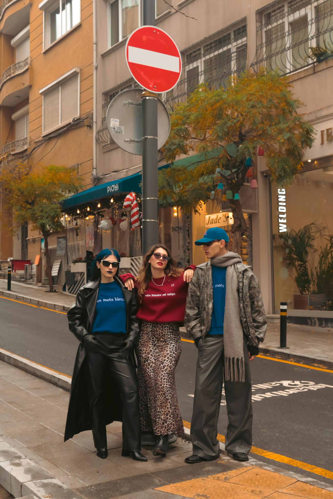 Three stylish friends pose on a fashionable street in fall attire.